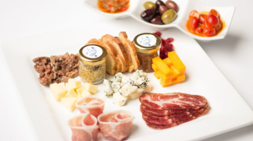 A gourmet platter featuring meats, cheeses, spreads, and olives, beautifully arranged on a white plate.