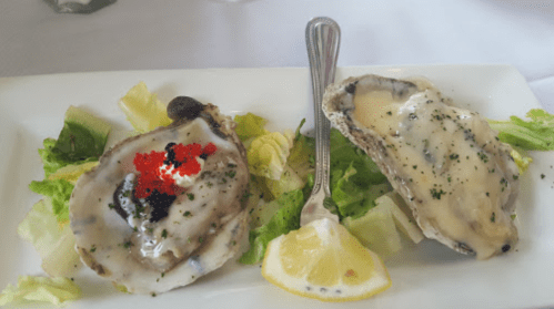 Two oysters on a bed of lettuce, one topped with red caviar and the other with a creamy sauce, garnished with lemon.