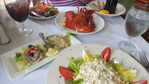 A table set with seafood dishes, including lobster, oysters, salad, and drinks, in a dining setting.