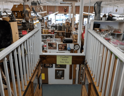 A view from a staircase overlooking a busy store filled with various items and decorations. A caution sign is visible.