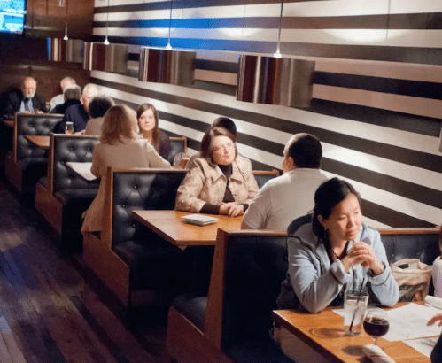 A dimly lit restaurant with striped walls, featuring diners in booths engaged in conversation.
