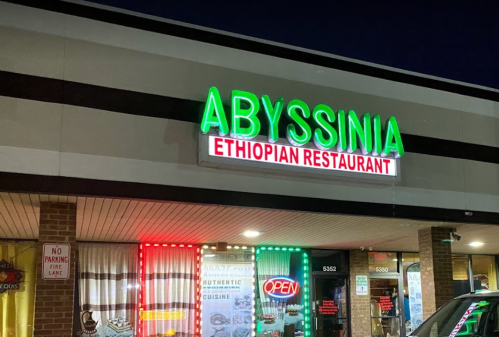 Sign for Abyssinia Ethiopian Restaurant, illuminated at night with "OPEN" in bright colors.