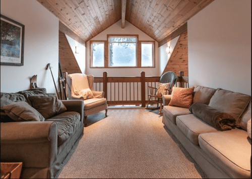 Cozy loft living area with two sofas, armchairs, and large windows under a wooden ceiling.