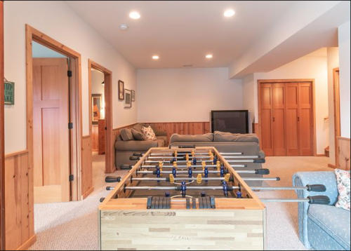 A cozy basement game room featuring a foosball table, sofas, and wooden doors.