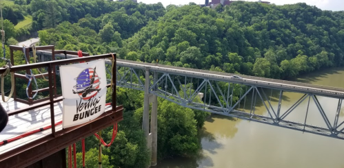 View from a bungee jumping platform overlooking a river and a bridge, surrounded by lush green trees.