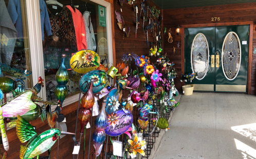 Colorful metal garden decorations displayed outside a shop with double doors and a wooden exterior.
