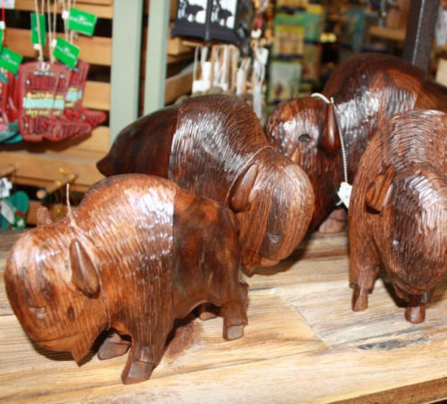 Wooden buffalo figurines displayed on a wooden shelf in a store.