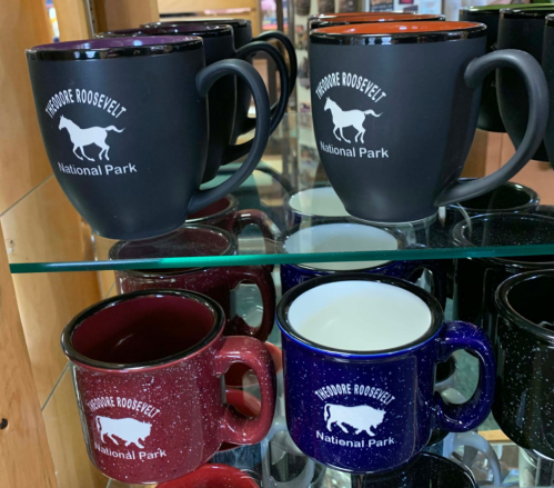 A display of mugs in various colors featuring "Theodore Roosevelt National Park" and a horse graphic.