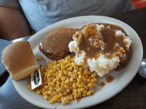 A plate of food featuring fried chicken, mashed potatoes with gravy, corn, and a dinner roll with butter.