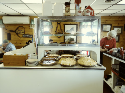 A cozy diner interior featuring a display of various pies and a staff member serving customers in the background.