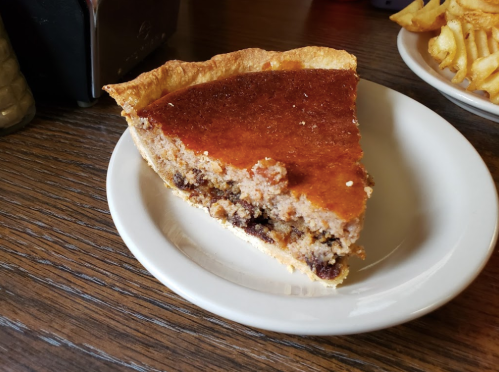 A slice of pie on a white plate, featuring a golden crust and a filling with visible chocolate chips.