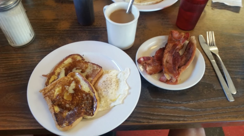 A plate with French toast, a fried egg, and a side of crispy bacon, with coffee in a cup nearby.