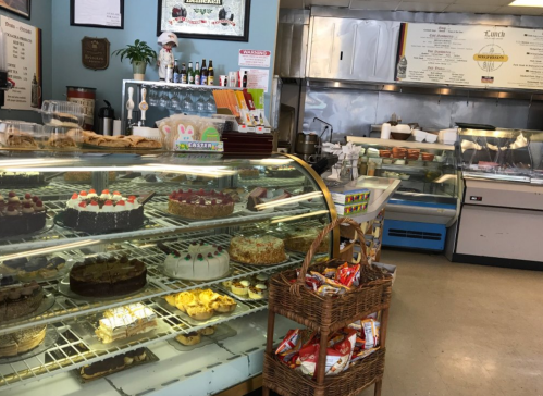 A display case filled with various cakes and pastries in a cozy bakery, with a menu board in the background.