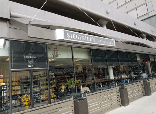 Exterior view of Siegfried's Delicatessen, featuring large windows and a modern awning, with a variety of products visible inside.