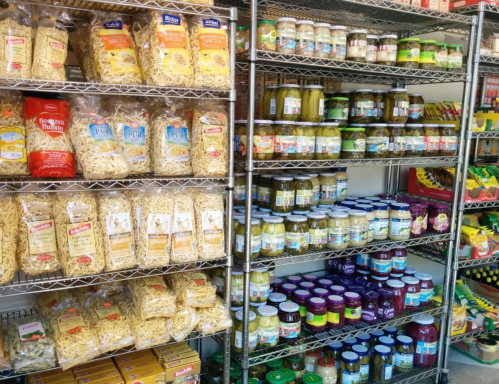 Shelves filled with various pasta, pickles, sauces, and canned goods in a grocery store.