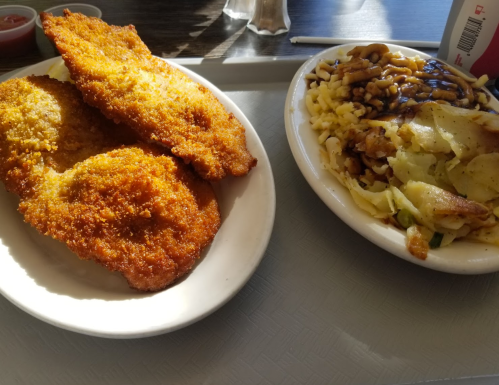 A plate with two golden-brown fried fillets and a bowl of creamy pasta topped with gravy.