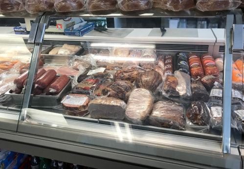 A display case filled with various packaged meats and deli products in a grocery store.