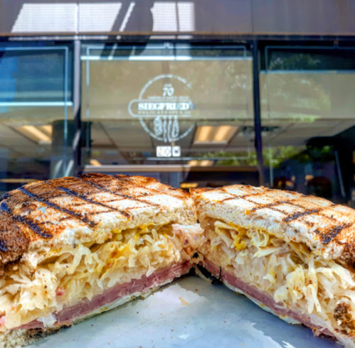 A close-up of a grilled sandwich filled with ham and sauerkraut, with a café window in the background.