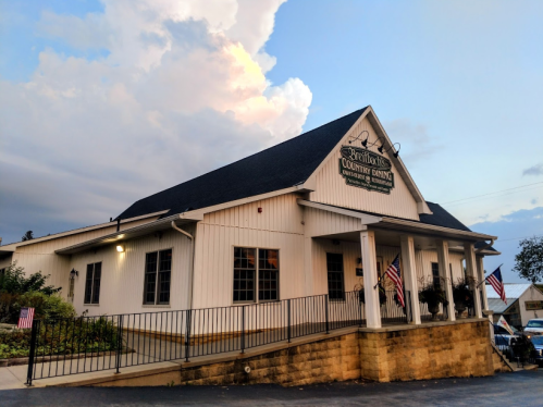 A white building with a black roof, featuring a sign for "Brooks Country Dining" and American flags on the porch.