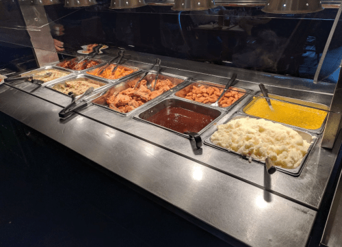 A buffet line featuring various dishes, including meats, sauces, mashed potatoes, and a yellow sauce.