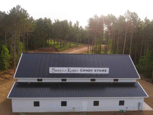 Aerial view of a candy store building surrounded by trees, featuring a sign that reads "Sweetly Kismet Candy Store."