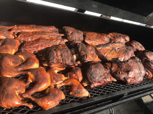 A variety of smoked meats, including ribs and chicken, sizzling on a grill with a smoky finish.