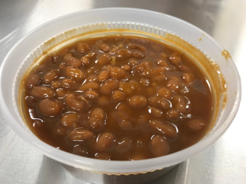 A plastic cup filled with baked beans in a thick, savory sauce.