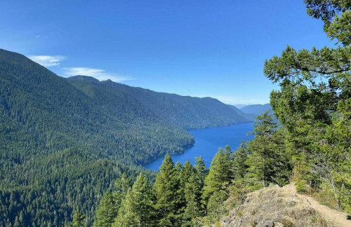 A scenic view of a blue lake surrounded by lush green mountains under a clear blue sky.
