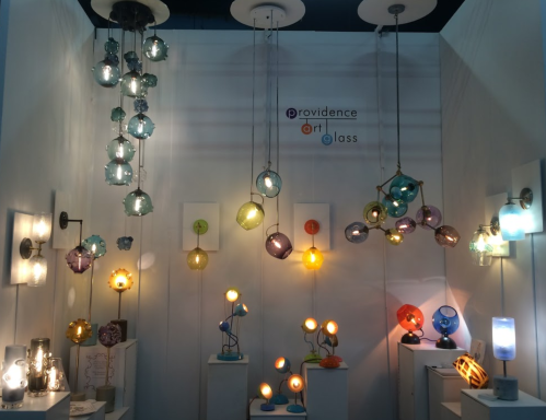 A display of colorful glass lamps and light fixtures hanging on a white wall, showcasing artistic designs.
