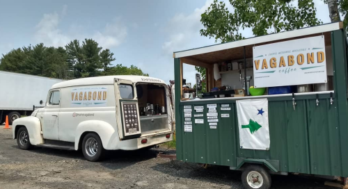 A vintage white truck and a green coffee stand with "Vagabond Coffee" signage in a sunny outdoor setting.