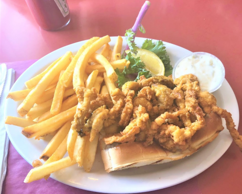 A plate of fried seafood on a bun, served with fries, a lemon wedge, and a side of dipping sauce.