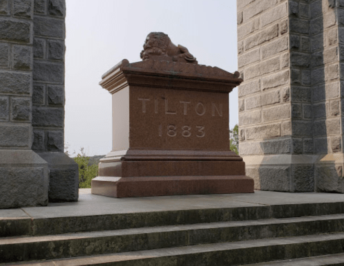 A granite monument with the name "TILTON" and the year "1883," flanked by stone pillars and steps.