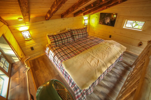 Cozy wooden bedroom with a plaid bedspread, sloped ceiling, and warm lighting.