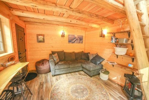 Cozy wooden interior of a tiny house featuring a sectional sofa, decorative shelves, and a warm atmosphere.
