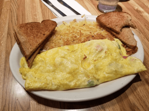 A plate with a fluffy omelet, crispy hash browns, and two slices of toasted bread.
