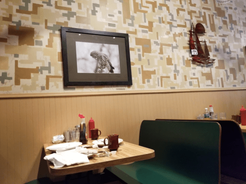 A cozy restaurant interior with green booths, a framed black-and-white photo on the wall, and condiment bottles on tables.
