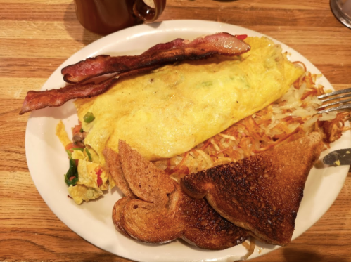 A plate of breakfast featuring an omelette, crispy bacon, hash browns, and toasted bread.