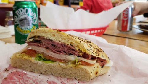 A close-up of a deli sandwich with layers of meat, lettuce, and tomato, alongside a can of Dr. Brown's soda.