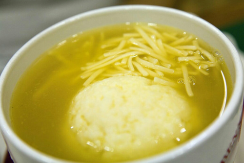 A bowl of clear broth with thin noodles and a round dumpling floating on top.