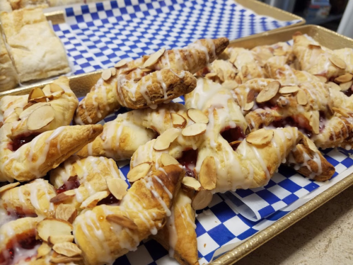 A tray of flaky pastries drizzled with icing and topped with sliced almonds, featuring a berry filling.