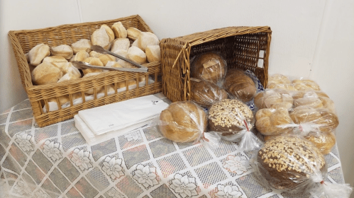 Baskets of assorted bread rolls and loaves, some wrapped in plastic, on a table with napkins.