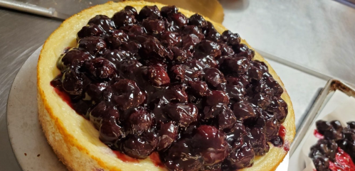 A close-up of a cheesecake topped with a glossy layer of dark cherries.