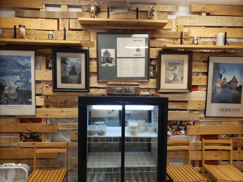 A rustic wall with wooden pallets, framed art, and a glass display fridge filled with jars.