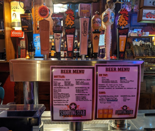 A bar counter displaying various beer taps and a menu with prices for bottles, cans, and draft options.