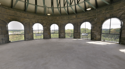 Interior view of a circular stone tower with multiple arched windows, offering a scenic view of the landscape outside.