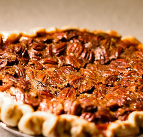 A close-up of a pecan pie with a golden crust and shiny, caramelized pecans on top.