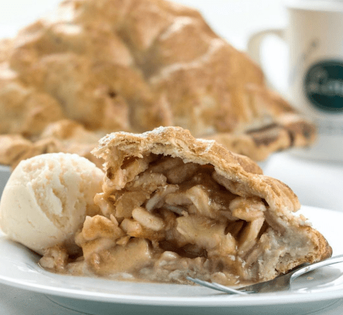 A slice of apple pie with a scoop of vanilla ice cream on a white plate, with a whole pie in the background.