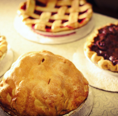 A variety of pies on display, including a golden-brown pie and a lattice-topped fruit pie in the background.