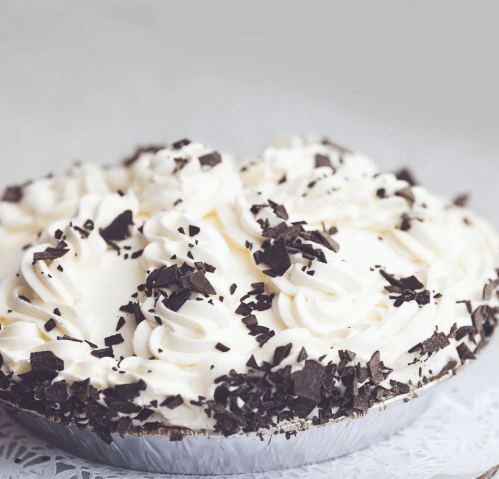 A creamy pie topped with swirls of whipped cream and chocolate shavings on a decorative lace surface.
