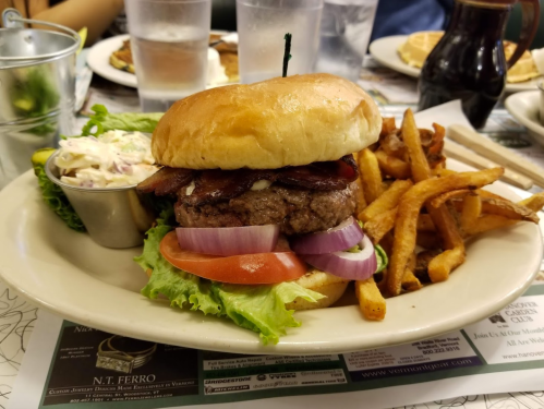 A juicy burger with bacon, lettuce, tomato, and onion, served with coleslaw and crispy fries on a plate.
